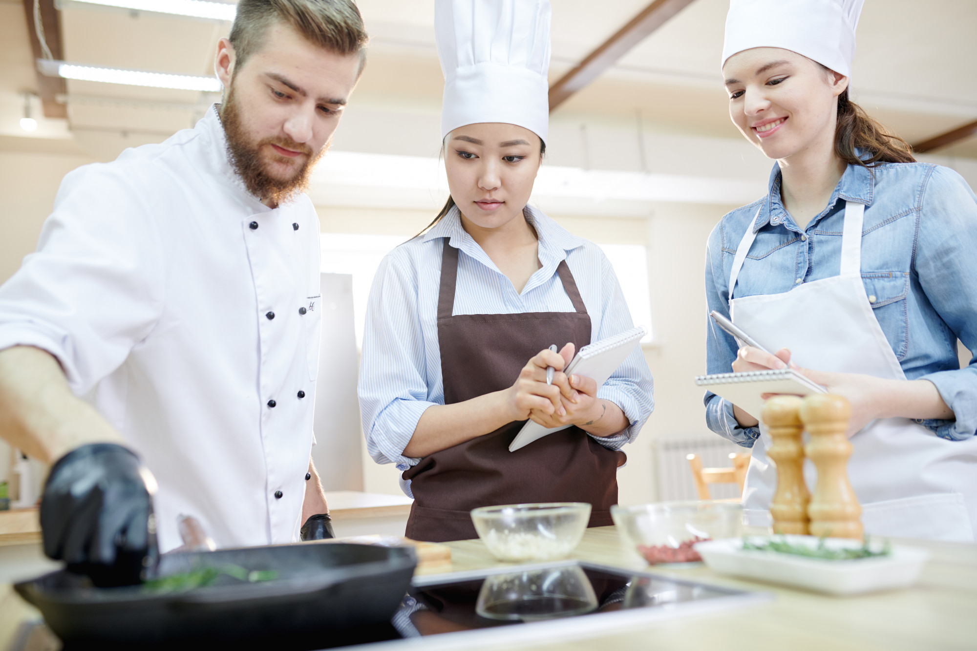 Students learning sauce technique around a large counter